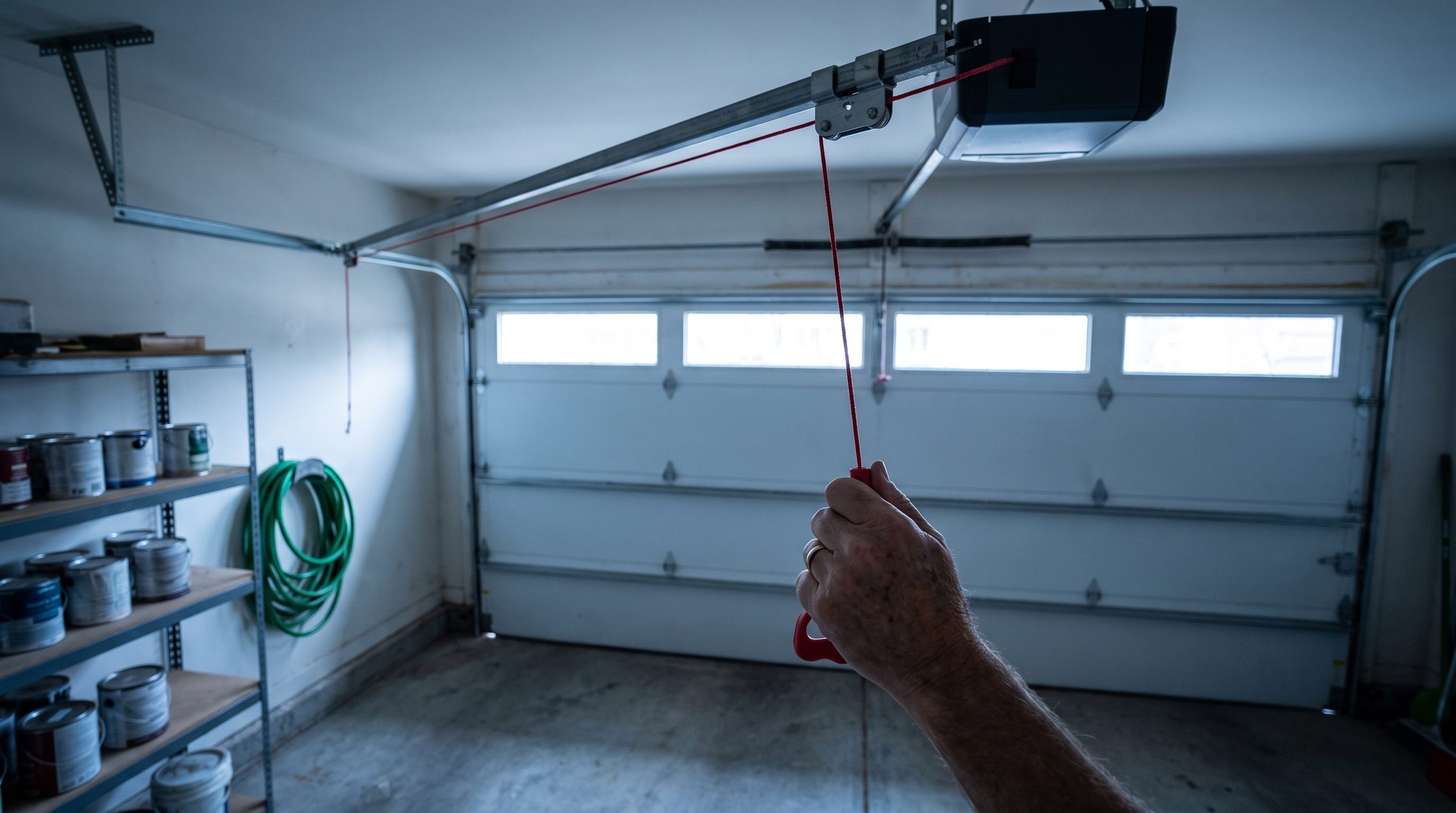 A hand gripping the red emergency release cord hanging from the rail of a garage door opener