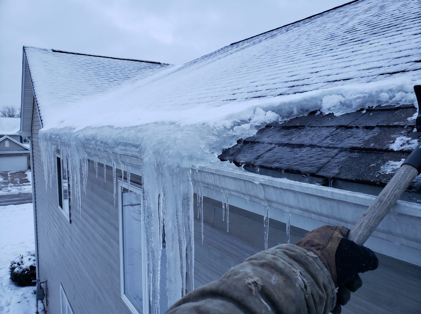 A thick ridge of ice along the lower edge of a shingled roof with heavy icicles