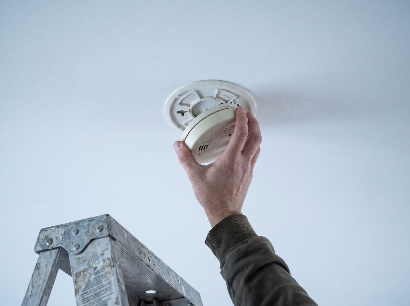 A hand twisting a round smoke alarm off its ceiling mount